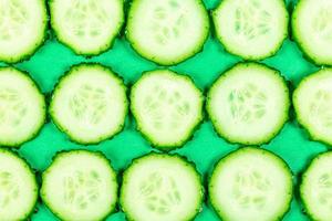 Sliced cucumber slices on a green background, top view