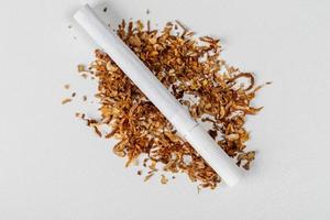 vista superior, cigarrillo encendido y tabaco seco sobre fondo blanco