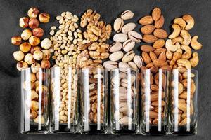 Top view, glasses with pistachios, almonds, cashews, walnuts, pine nuts and hazelnuts on a black background