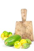 Exotic fruit on a white background with old kitchen board. Yellow passion fruit, papaya, cactus fruit, limes and lemons photo