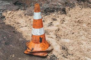 Orange and white striped cone on an asphalt pavement repair site photo