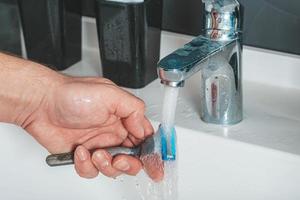 A man washes a razor under the faucet in the bathroom photo