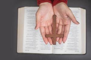 manos de mujer rezando con una biblia y una cruz de madera.