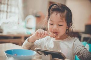niña asiática feliz comiendo y viendo vdo desde el teléfono inteligente. foto