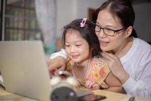 mujer asiática enseñando a su duagther con computadora portátil y concepto de estudio en línea de teléfono inteligente. foto