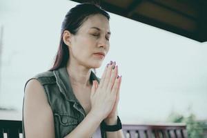mujer asiática rezando por la mañana al aire libre, con las manos dobladas en el concepto de oración por la fe, la espiritualidad y la religión, el concepto en línea de los servicios de la iglesia. foto