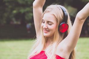 joven rubia sonriendo feliz usando auriculares en el parque.