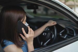 una mujer asiática que usa un teléfono móvil mientras conduce una mujer llama al seguro oa alguien para que la ayude cuando el automóvil se descompone o tiene un accidente. foto