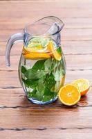Jug with orange and mint lemonade on a wooden background photo