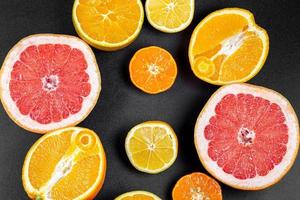 Fruit background with half a grapefruit, orange, lemon and mandarin on a black background, top view