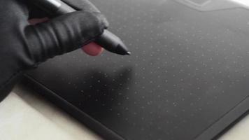 la mano de un diseñador en un guante negro se basa en el espacio de trabajo de una tableta gráfica, de cerca.