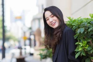 Portrait Asian woman with long hair wears black coat and stands outdoor in town. photo