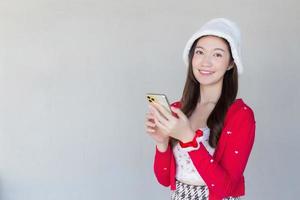 Portrait of a pretty Asian woman wearing a red dress and white hat happily using a smartphone on a white background. photo