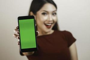 joven asiática feliz y sonriente mostrando y señalando una pantalla verde en blanco. foto