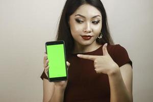 Happy and smiling young Asian woman showing and pointing to a green blank screen. photo