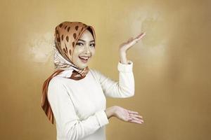 Cheerful young Muslim Asian woman pointing side to copy space with smile photo