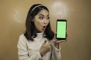 Asian beautiful girl is shocked show green screen in smartphone with white shirt photo