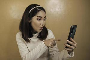 hermosa chica asiática está sorprendida en el teléfono inteligente con camisa blanca foto