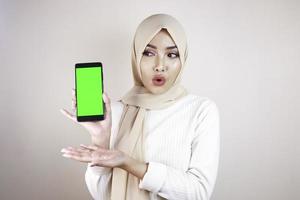 Young Asian Muslim beautiful girl wearing head scarf is shocked showing green screen smartphone photo