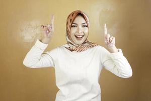 Cheerful young Muslim Asian woman pointing above to copy space with smile photo