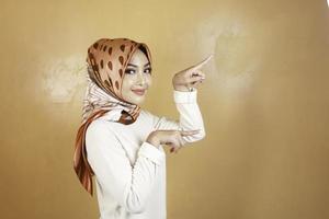 Cheerful young Muslim Asian woman pointing side to copy space with smile photo