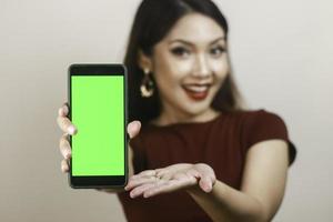Happy and smiling young Asian woman showing and pointing to a green blank screen. photo