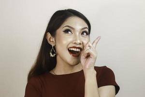 Shock face of a young Asian woman wearing a red shirt pointing upwards. Advertisement concept. photo