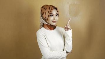 Cheerful young Muslim Asian woman pointing above to copy space with smile photo