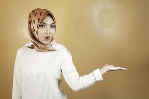 Shock face of young Muslim Asian woman pointing side to copy space photo