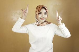 Cheerful young Muslim Asian woman pointing above to copy space with smile photo