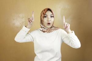 Cheerful young Muslim Asian woman pointing above to copy space with smile photo