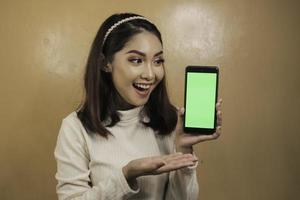 mujeres asiáticas jóvenes felices y sonrientes que muestran una pantalla en blanco verde. foto