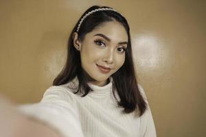 Young Asian woman is smiling and selfie taking pictures with her mobile phone. Indonesian woman on orange background. photo