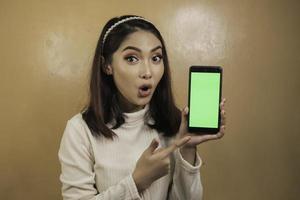 Asian beautiful girl is shocked show green screen in smartphone with white shirt photo