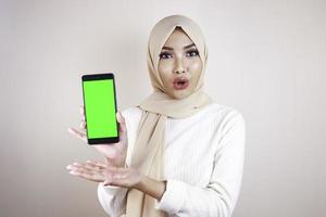 Young Asian Muslim beautiful girl wearing head scarf is shocked showing green screen smartphone photo