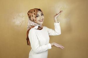 Cheerful young Muslim Asian woman pointing side to copy space with smile photo