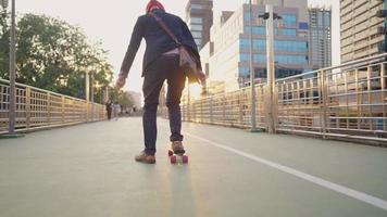 joven hombre de negocios deslizándose en el monopatín, estilo de vida urbano de transporte alternativo, evitar atascos de tráfico abarrotados durante la hora pico, destello de lente natural al atardecer, vista desde atrás, tiro de ángulo bajo video