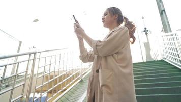 atractiva turista asiática rubia caminando por el paso elevado en la ciudad de verano, yendo por ruta, usando la aplicación de navegación en línea con mapa en el teléfono inteligente, cerrar gesto de búsqueda, tecnología en la vida diaria