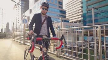 joven hombre de negocios lleva una bicicleta en el paso elevado de la ciudad, usando su propia bicicleta, negocio y medio ambiente del concepto de transporte, edificio moderno de cristal de reflejo solar en el fondo. paisaje urbano.