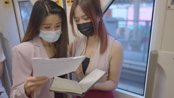 Female office colleague friends wear protective face mask look at paper document works standing inside metro subway train, work cooperative, public transport, women in business attire city lifestyle video