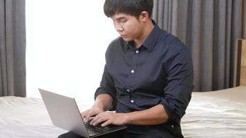 asiatischer gutaussehender geschäftsmann im formellen hemd sitzt auf der bettkante und tippt auf computer-laptop, studenten-fernunterricht auf virtueller distanz online-lektion, mann, der zu hause videokonferenz-chat macht video
