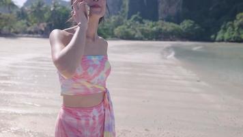 Asian lady having phone call standing on island beach, sea shore, calm low tide waves communication technology connecting people, summer holiday vacation, long distanced relationship, keep in touch video