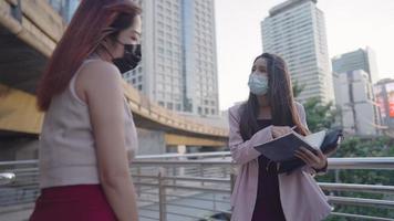 Two asian female office workers discuss work outside the building, busy supervisor giving her intern advice project brief , colleagues best friend relationship, work environment, city skyscraper
