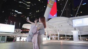mulher asiática feliz fazendo uma chamada de vídeo selfie com seu smartphone mostrando uma boa vida depois de fazer compras no centro da cidade, destino de viagem na ásia, luz noturna da cidade, estilo de vida urbano elegante video