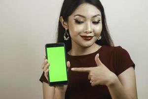 joven asiática feliz y sonriente mostrando y señalando una pantalla verde en blanco. foto