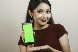 Happy and smiling young Asian woman showing and pointing to a green blank screen. photo