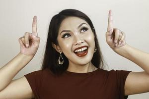 Shock face of a young Asian woman wearing a red shirt pointing upwards. Advertisement concept. photo