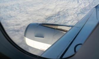 View from inside plane through a plane window over white clouds. Window view of the plane sees an airplane engine. Airplane flying in the sky. Commercial airline flight. Travel abroad after covid-19. photo