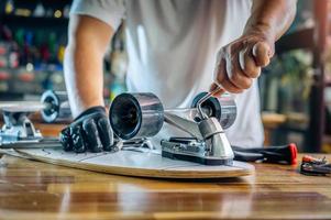man use the socket tool or hex keys to remove the nuts on skateboard and adjusts suspension in workshop, Skateboard maintenance and repair concept. Selective focus on suspension set photo