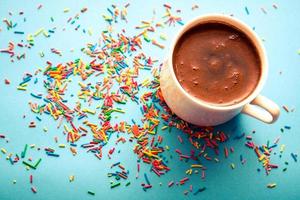 una taza de café negro caliente sobre fondo azul con coloridos chispitas de azúcar. foto